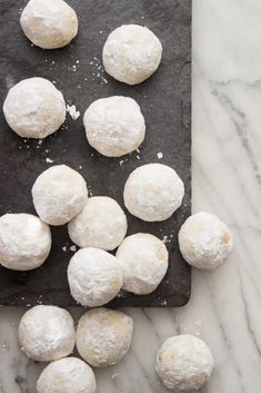 doughnuts are on a black cutting board with powdered sugar scattered around them