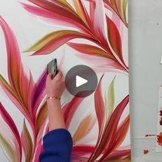 a person is painting on a wall with red and green leaves