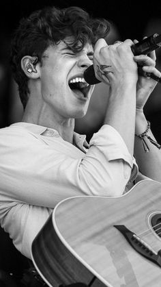 a young man singing into a microphone while holding an acoustic guitar in his right hand