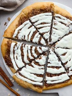 a sliced pizza with white icing on a plate next to cinnamon sticks and an orange napkin