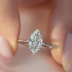 a woman's hand holding a ring with a pear shaped diamond in the center