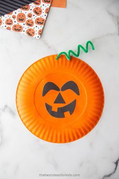 an orange paper plate with a jack o lantern design on it and halloween decorations in the background