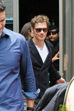 two men in suits and sunglasses are walking out of a building with people behind them