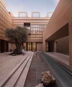 a woman is standing in the middle of a courtyard with stairs leading up to an olive tree