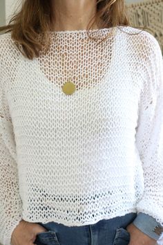 a woman wearing a white top with a gold disc on it's chest and her hands in her pockets