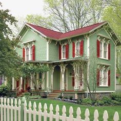 a green house with red shutters and a white picket fence in front of it