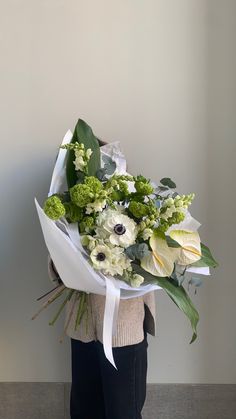 a woman holding a bouquet of white and green flowers in her hands while standing against a wall