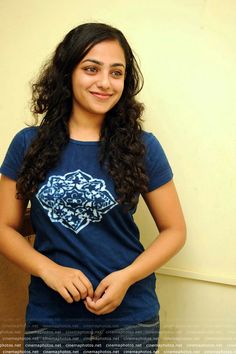 a woman standing in front of a wall wearing a blue shirt