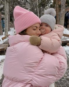 a woman holding a baby in her arms while wearing a pink coat and beanie