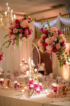 two tall vases filled with pink flowers and greenery on top of a table