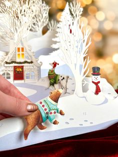 a hand is holding an ornament in front of a christmas scene