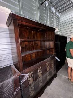 two men are looking at an old wooden dresser in a storage room with metal walls