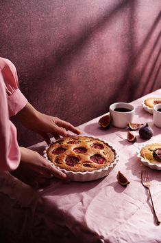 a person holding a pie on top of a table next to cups and utensils