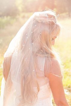 a woman in a wedding dress is walking through the grass with her veil over her head