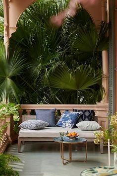 an outdoor seating area with tropical plants on the wall, and a bench in front of it