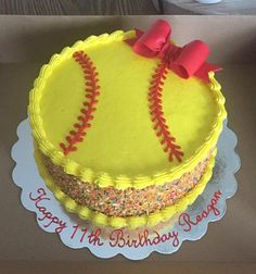 a birthday cake decorated with a softball ball and red bow on top is sitting in a box