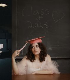 a woman sitting at a table with a graduation cap on her head and writing on the chalkboard behind her