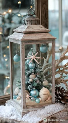 a small christmas tree in a glass container on top of snow covered ground next to a mirror