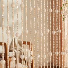 beads hanging from the ceiling in front of a window with curtains on it and a chair next to it