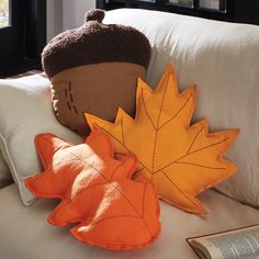 two decorative pillows are sitting on a couch with an orange and brown leaf shaped pillow