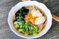 a bowl filled with noodles and vegetables next to chopsticks on a wooden table