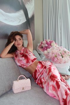 a beautiful woman laying on top of a couch next to a pink purse and flowers