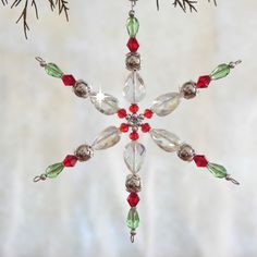 a snowflake ornament hanging from a tree branch with red and green beads