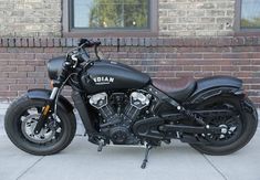 a black motorcycle parked on the sidewalk in front of a brick wall and windowed building