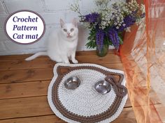 a white cat sitting on top of a wooden floor next to two bowls and spoons