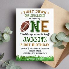 a first birthday party card with a football on it and greenery next to it