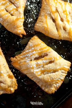 four pieces of pie sitting on top of a black pan covered in powdered sugar