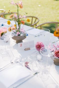 the table is set with flowers in vases and place cards for guests to use