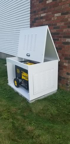 a white box sitting in the grass next to a brick building with a door open