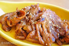 a yellow plate topped with meat covered in sesame seeds and seasoning on top of a wooden table