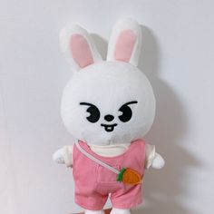 a white stuffed rabbit with pink overalls and a carrot in its hand on a table