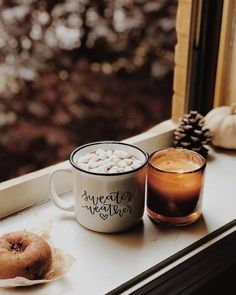 two coffee mugs sitting on a window sill with marshmallows and a donut