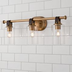 three lights are hanging on the wall next to a white brick wall in a bathroom