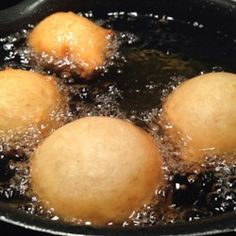 three balls of bread frying in oil in a pan