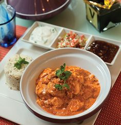 a bowl of food on a plate with rice, sauce and other foods in the background