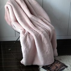 a pink blanket sitting on top of a wooden floor next to a chair and book