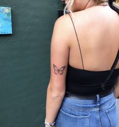 a woman with a butterfly tattoo on her left upper arm and lower arm, standing next to a green wall