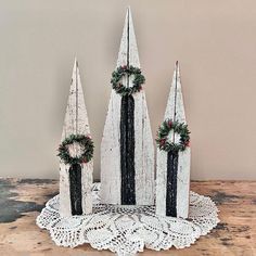 three wooden christmas trees with wreaths on them sitting on top of a doily