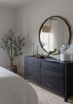 a bedroom with a large round mirror on the wall and dresser in front of it