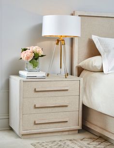 a nightstand with flowers on it next to a bed