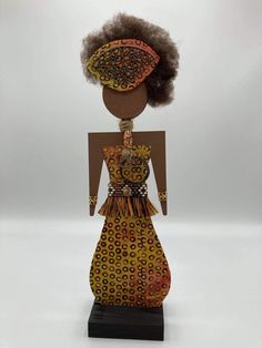 an african doll is standing on a black base and wearing a dress with brown trim