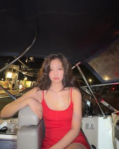 a woman in a red dress is sitting on a boat and posing for the camera