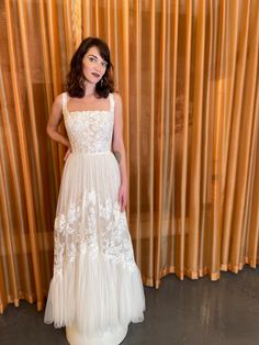 a woman standing in front of a curtain wearing a white dress