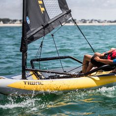 two people in a yellow sailboat on the water with one person wearing a life jacket