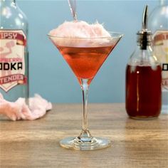 a pink drink in a martini glass next to two bottles of booze and ice cream