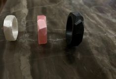 three rings sitting on top of a table next to each other, one black and one pink